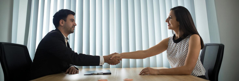 we can see a man and a women shaking hands by sitting from there chair on either side of the table